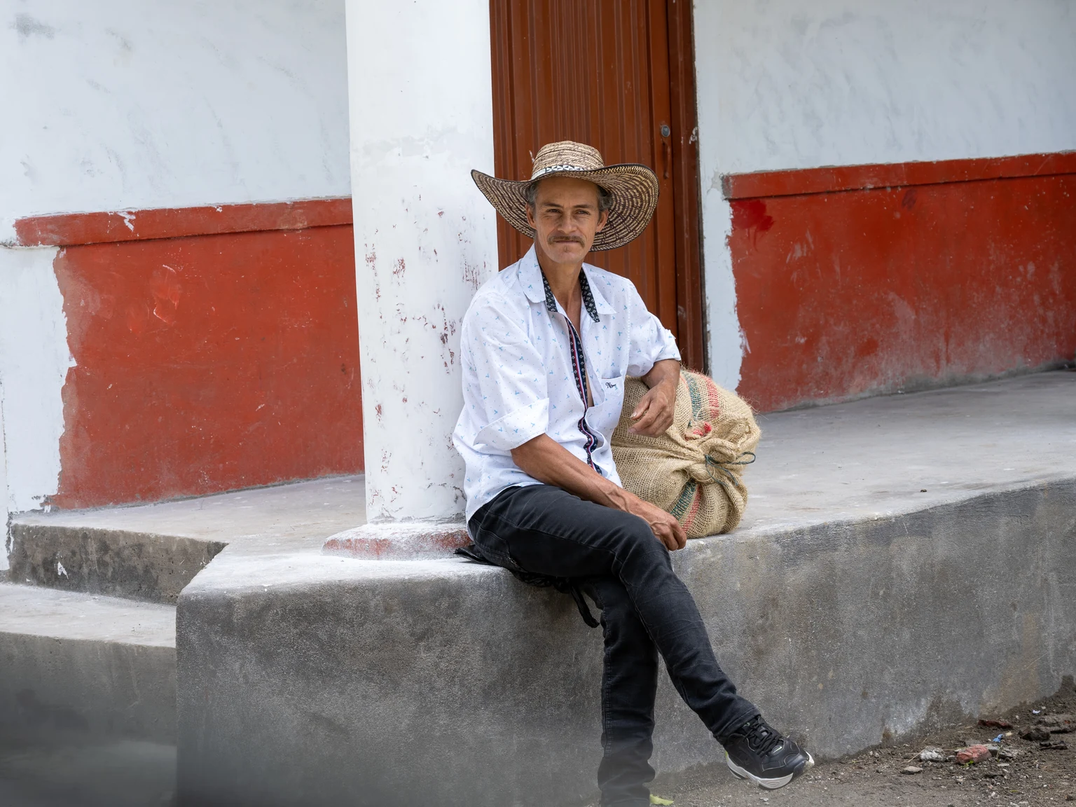 Campesino cafetero en Colombia, con sombrero y un costal, esperando transporte al pueblo